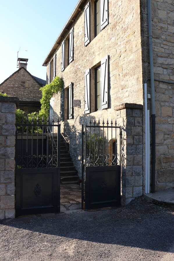 Un bâtiment en pierre doté d’une entrée fermée par un portail, d’un escalier et surplombant un ciel dégagé.