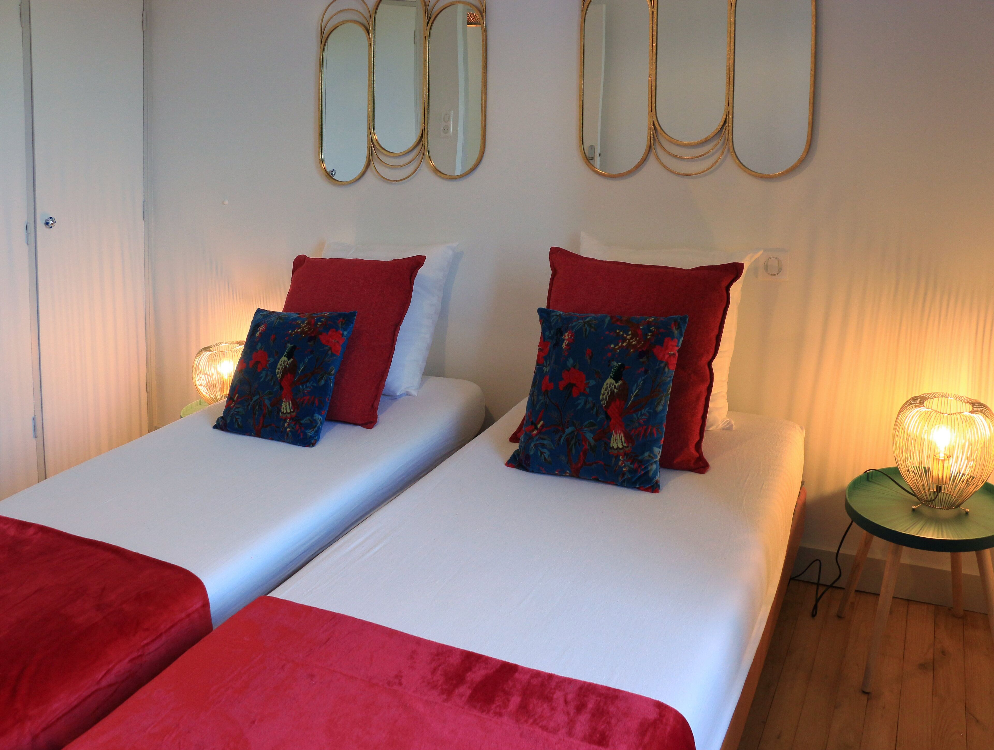 A double bed with red and blue floral pillows, a small bedside table with a lamp, and a mirror on the wall.