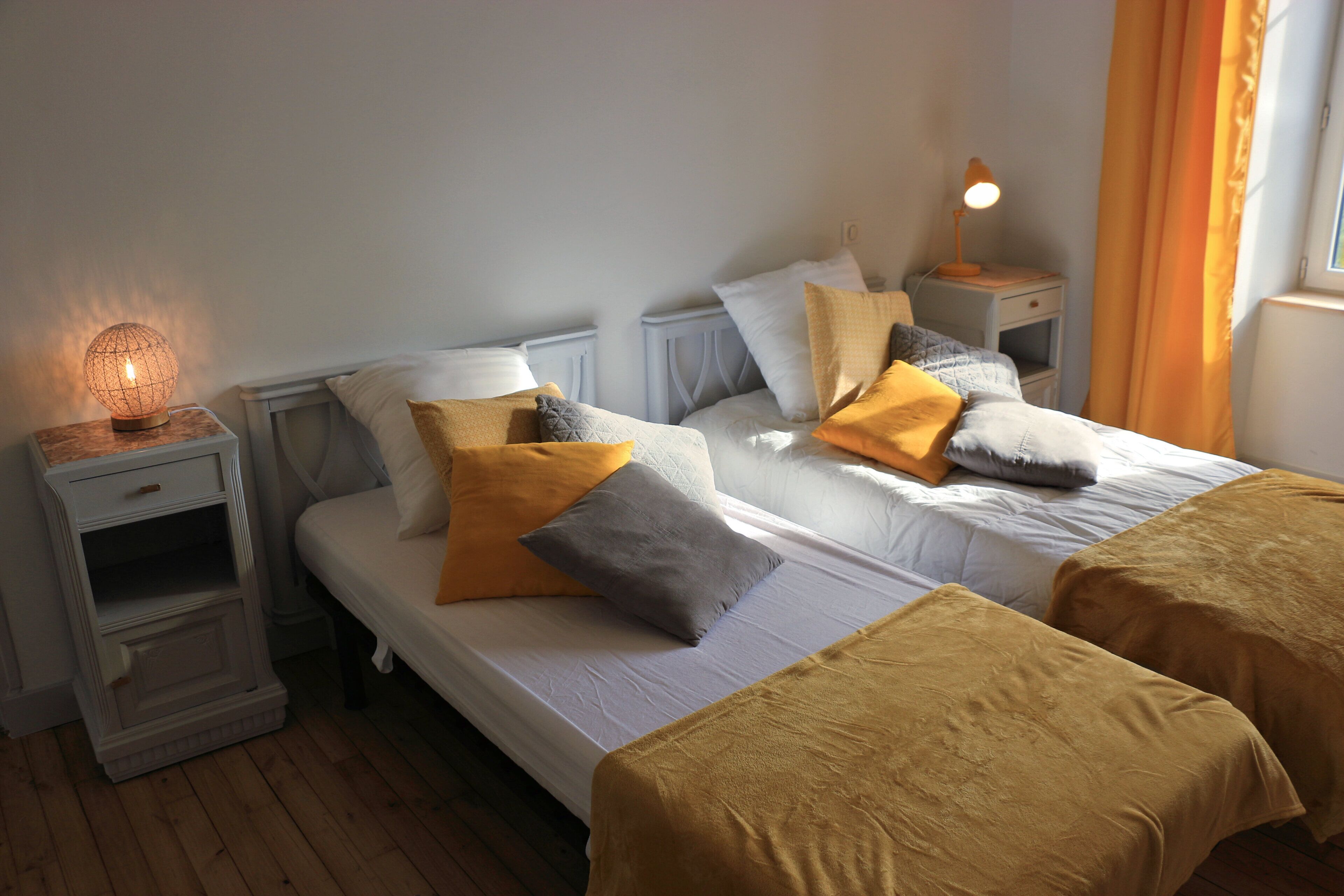 A bedroom with two beds, a nightstand with a lamp, a dresser, and a window with curtains.