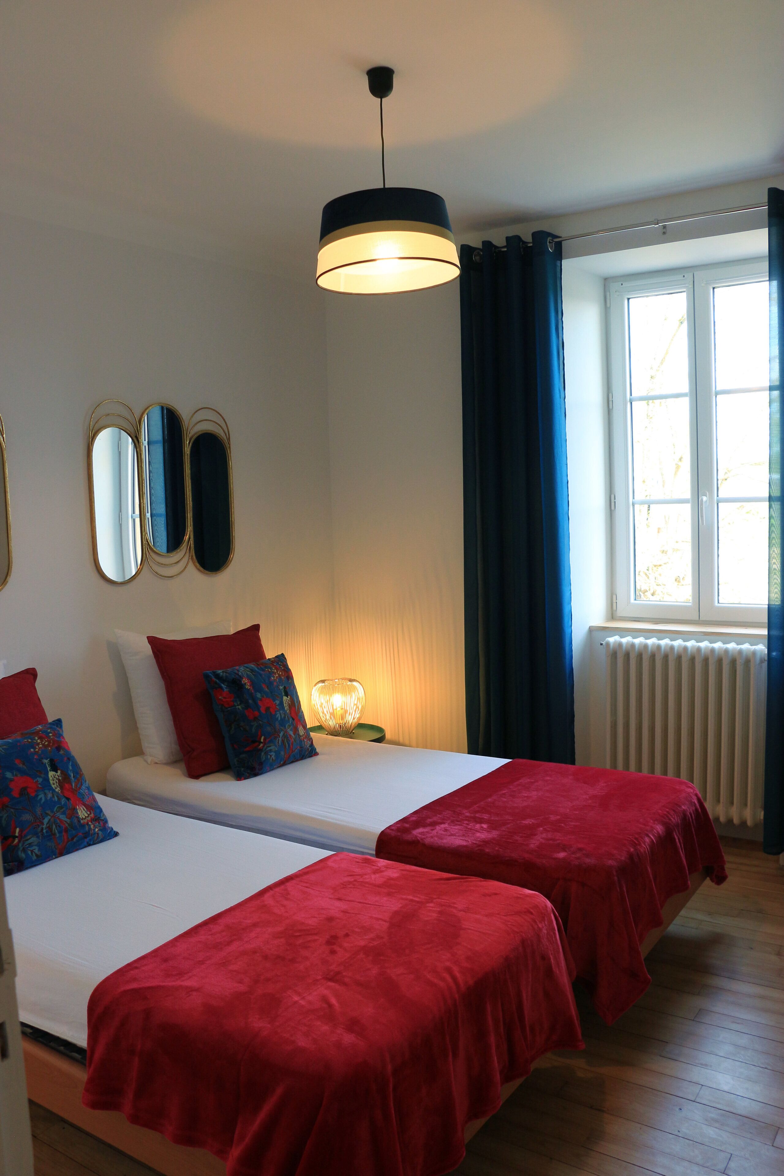 A room with two beds, a window with curtains, a radiator, and a hanging light fixture.
