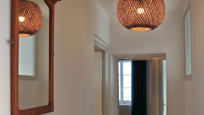A hallway with wooden flooring, a mirror on the left, and a hanging light fixture.