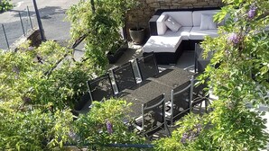A patio area with a white outdoor sofa, a stone wall, and various plants.