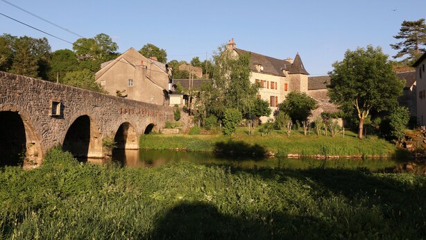 A stone bridge over a calm river, surrounded by lush greenery and historic buildings.