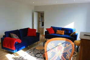 Un salon avec deux canapés bleus, un fauteuil à motifs et une petite table ronde.