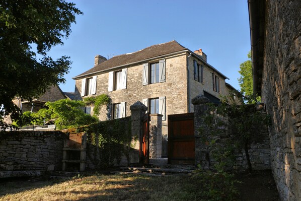 A stone building with a large wooden door and multiple windows. - "Le gîte de la glycine," a renovated house with a terrace offering a magnificent view and a fenced-in garden (Palmas d'Aveyron)
