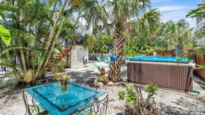 Un patio trasero con una mesa de vidrio, un jacuzzi y diversas plantas tropicales.
