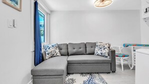 Una sala de estar moderna con un sofá seccional gris, un tapete estampado y un comedor con una mesa y sillas blancas.
