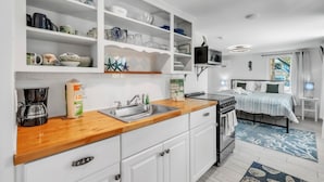 Una cocina compacta con armarios blancos, encimera de madera y microondas integrado.