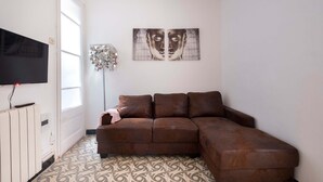 A living room with a brown sectional sofa, a flat-screen TV mounted on the wall, a decorative floor lamp, and a large abstract painting. - Apartment (Barcelona)