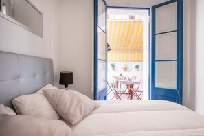 A bedroom with a bed, a bedside lamp, and a view of an outdoor dining area through an open door.