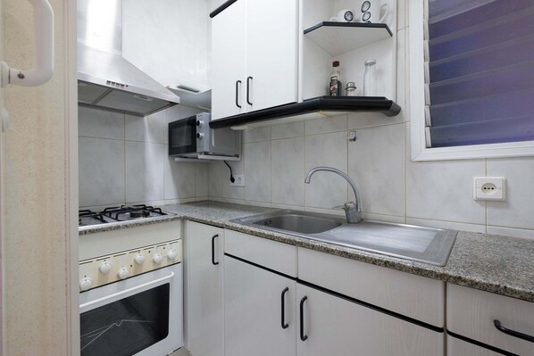 A kitchen with white cabinets, a stainless steel sink, a gas stove, and a microwave.