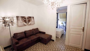 A living room with a brown sectional sofa, a floor lamp, and wall art. There is a door leading to another room with a table and chairs. - Apartment (Barcelona)
