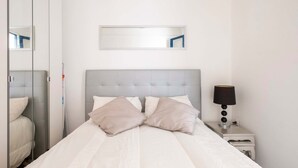 A neatly made bed with a grey headboard, a bedside lamp, and a mirror on the wall. - Apartment (Barcelona)