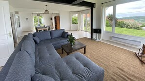 A spacious living room with a large sectional sofa, a coffee table, and a view of the outdoors through large windows. - House (Criel-sur-Mer)