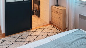 A modern bedroom with a bed, a bedside table, a lamp, and a view of the outdoors through a window. - House (Criel-sur-Mer)