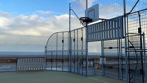 A tennis court with a net, surrounded by a metal fence, and a basketball hoop in the background. - House (Criel-sur-Mer)