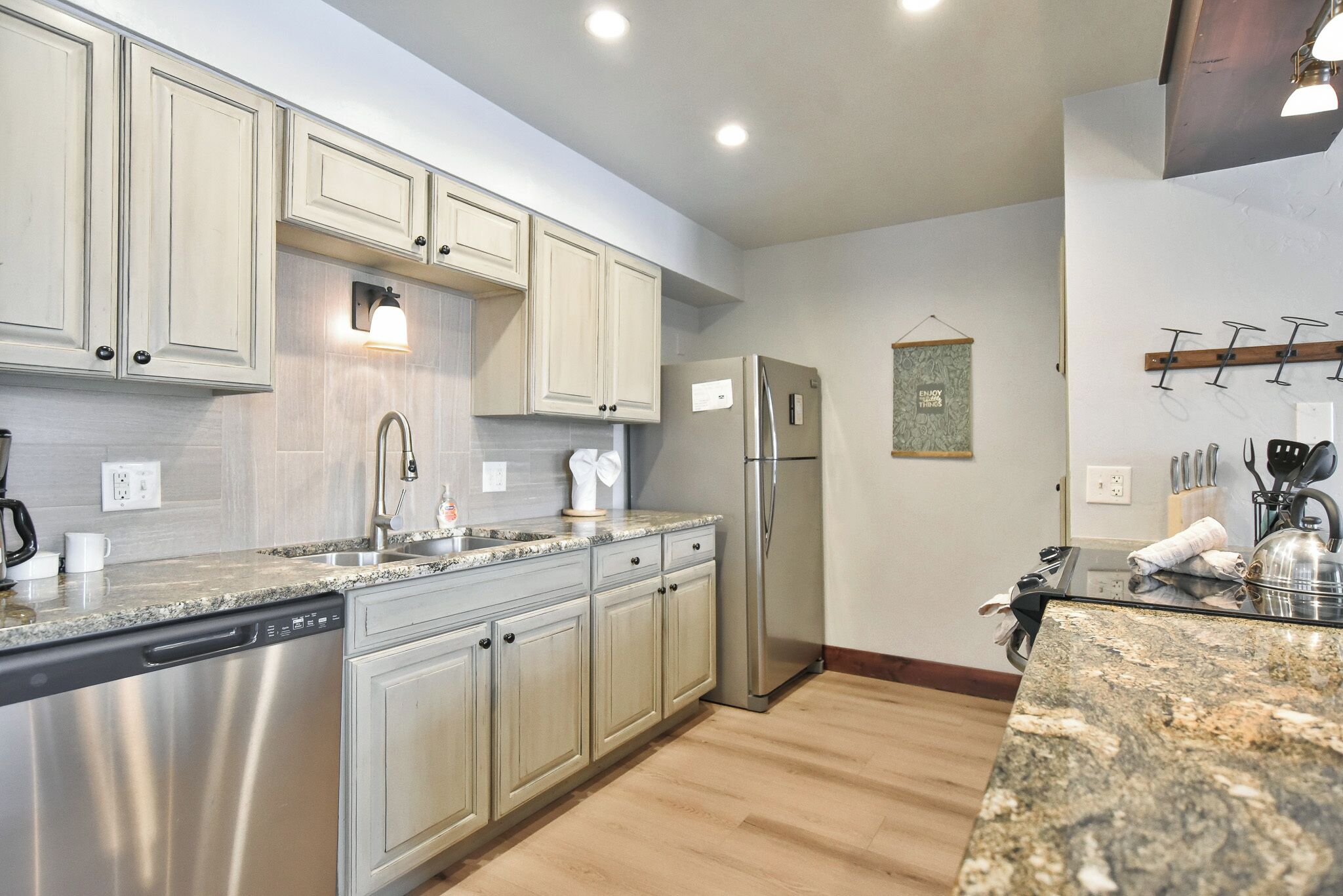 A kitchen with light-colored cabinets, stainless steel appliances, granite countertops, and a wooden floor.