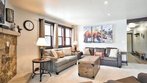 A cozy living room with a stone fireplace, two sofas, a coffee table, and a large window with curtains. - Park Place Peak 10 Condo: Walk To Lift, Main Street (Breckenridge)