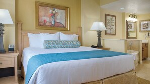 A hotel room with a large bed, a nightstand with a lamp, a dresser, a vanity with a mirror, and a painting on the wall. - 2 bedroom, resort amenities, Disney convenient location!  (Lake Buena Vista)