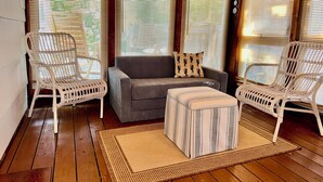 A cozy room with a grey sofa, two wicker chairs, a striped ottoman, and a wooden floor. - 13 Collins Street, Unit B, Dewey Beach, Delaware (Dewey Beach)