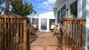 A wooden deck with two chairs and a small table, leading to a house with large windows and a door.