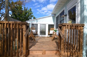 A wooden deck with two chairs and a small table, leading to a house with large windows and a door.