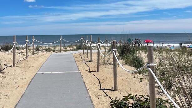 A beach pathway leading to the ocean with a rope barrier, sandy beach, and a clear sky.