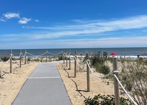 A beach pathway leading to the ocean with a rope barrier, sandy beach, and a clear sky.