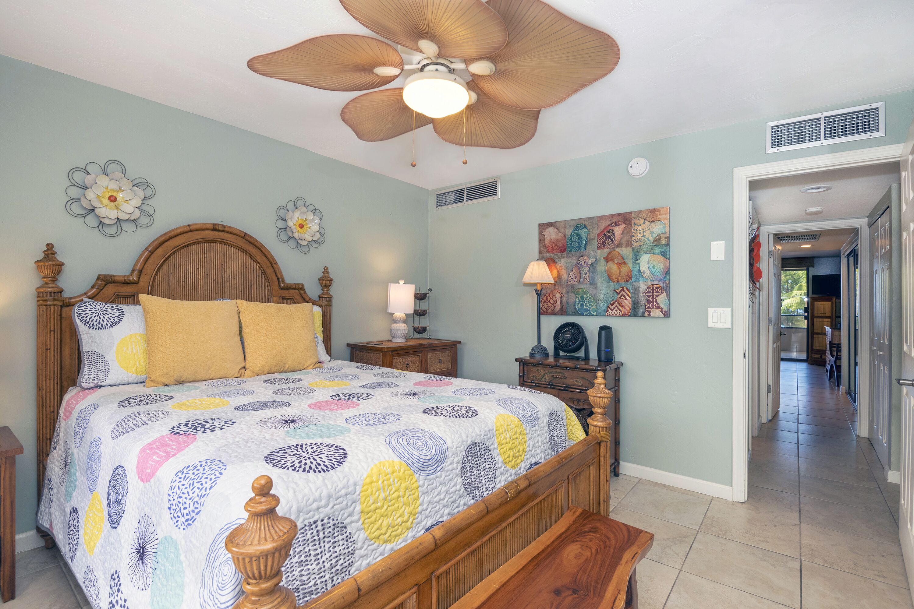 A bedroom with a wooden bed, a ceiling fan, a nightstand, and a wall art piece.
