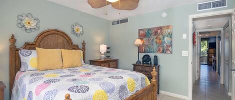 A bedroom with a wooden bed, a ceiling fan, a nightstand, and a wall art piece.