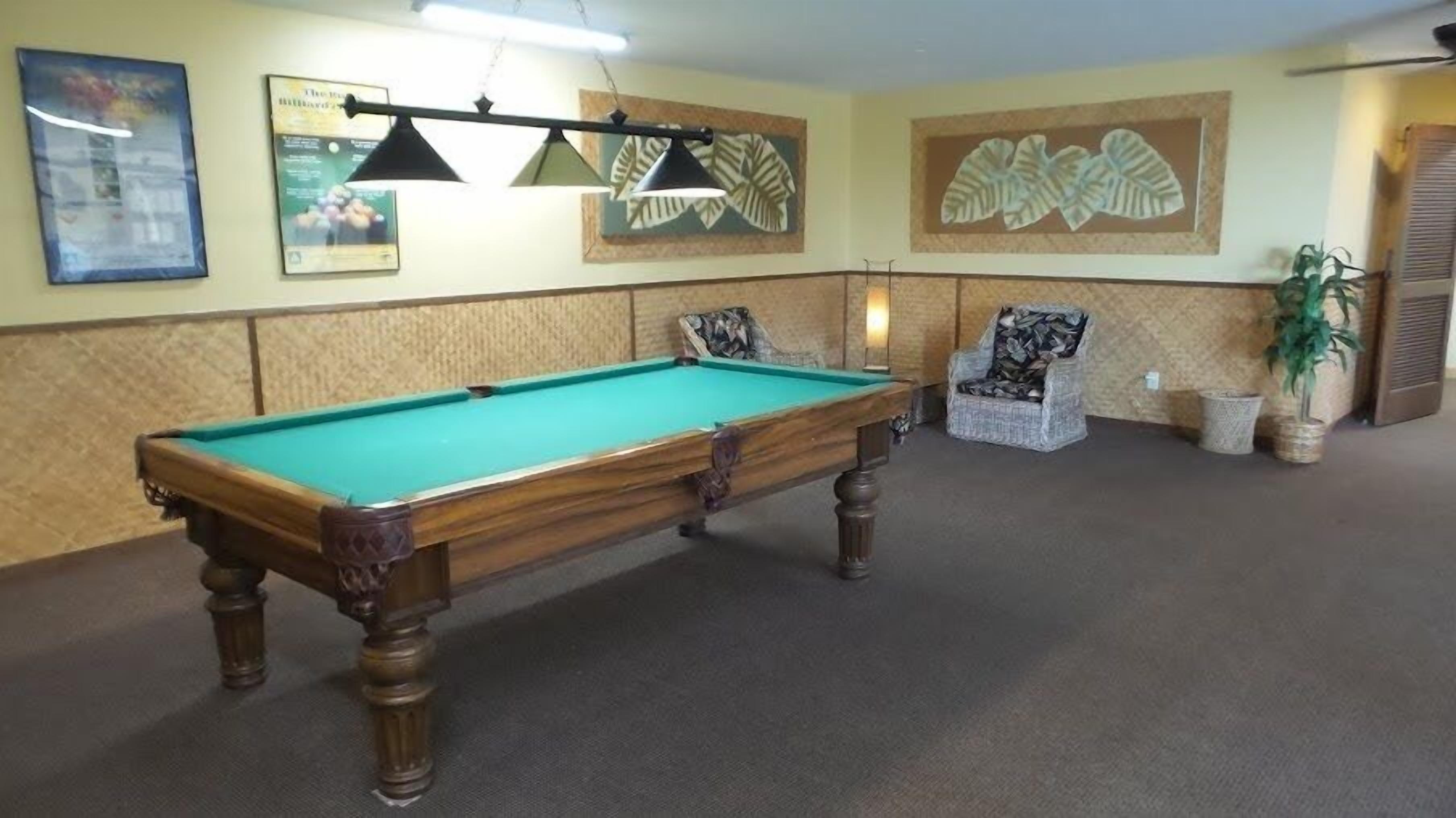 A pool table in a room with a textured wall, two chairs, and a potted plant.