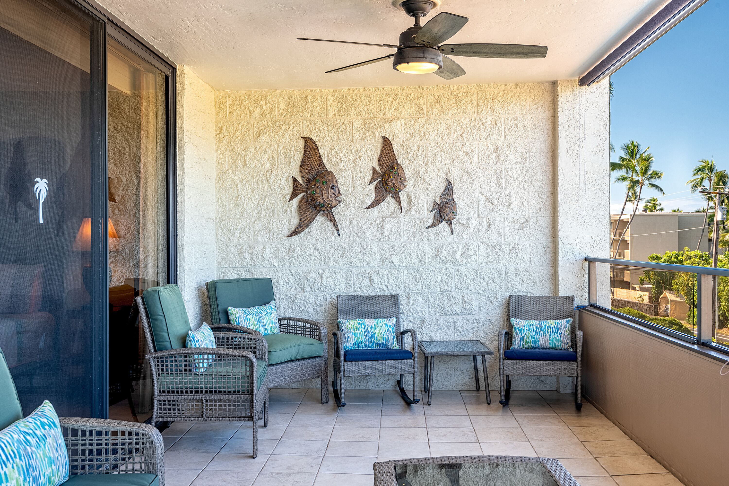 Ein Balkon mit Korbmöbeln, einem Deckenventilator und Fisch-Wandbildern.