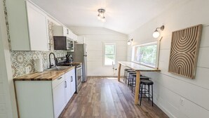A kitchen with white cabinets, a wooden countertop, a refrigerator, and a dining area with stools. - The Crash Pad ~ Riverfront Retreat with Gameroom (Izard County)