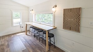 A kitchen with a wooden table and bar stools, a window with a view, and a decorative wall piece. - The Crash Pad ~ Riverfront Retreat with Gameroom (Izard County)