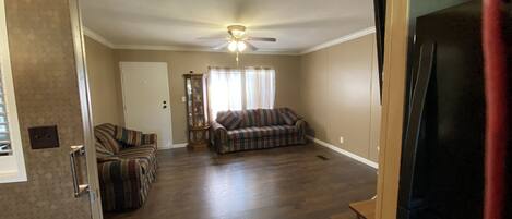 A spacious living room with hardwood floors, a ceiling fan, and a plaid sofa.