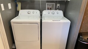 Une buanderie équipée de deux machines à laver et de deux sèche-linge à chargement frontal superposés, d’une poubelle et d’une prise électrique au mur.
