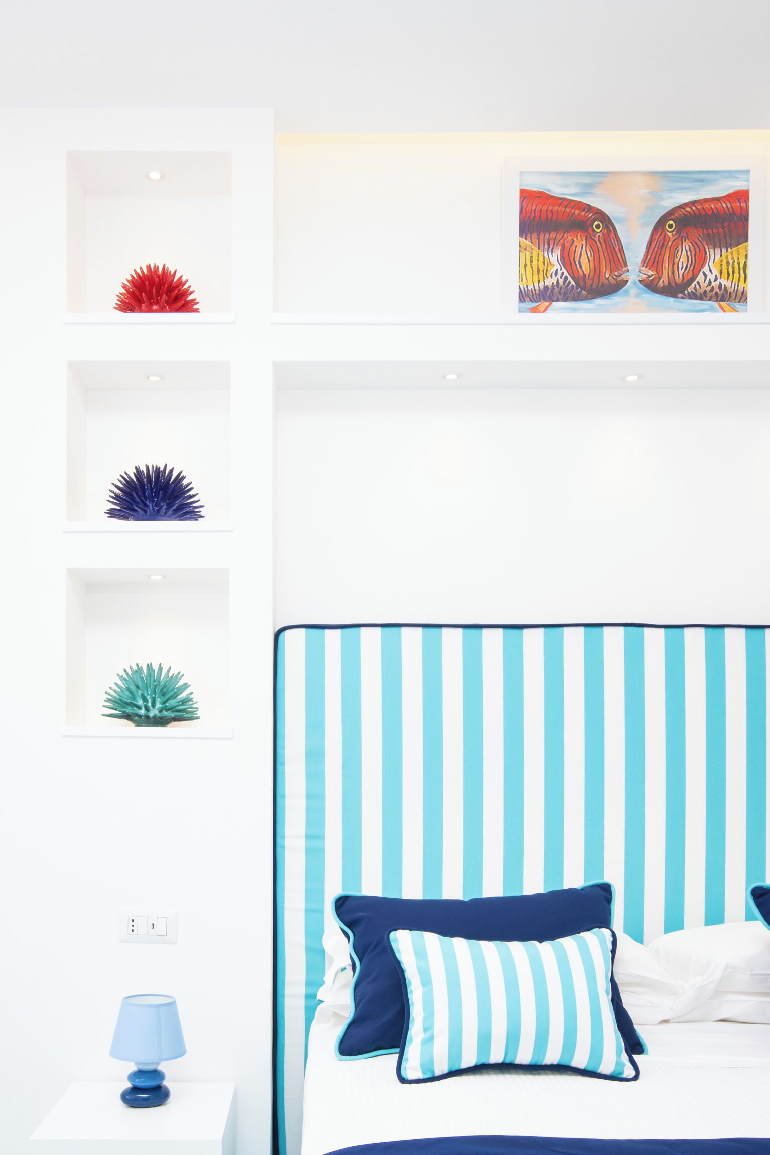 A bedroom with a striped headboard, a bed with blue and white striped pillows, and decorative items on shelves.