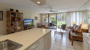 A spacious living area with a kitchen, dining set, and a large window offering a view of the outdoors. - Ground Floor Maui Sunset B105 on the oceanfront in Kihei (Kihei)