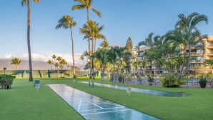 A well-maintained courtyard with a shuffleboard court, palm trees, and a building with balconies in the background. - Ground Floor Maui Sunset B105 on the oceanfront in Kihei (Kihei)