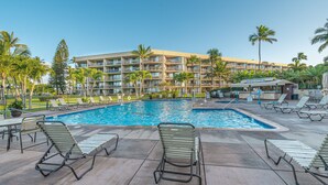 A hotel pool area with lounge chairs, palm trees, and a building with multiple balconies. - Ground Floor Maui Sunset B105 on the oceanfront in Kihei (Kihei)