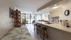 A modern kitchen with a bar area, a dining area with chairs, and a large window providing a view of the outdoors. - Ground Floor condo suite with pool and ocean access (Kihei)