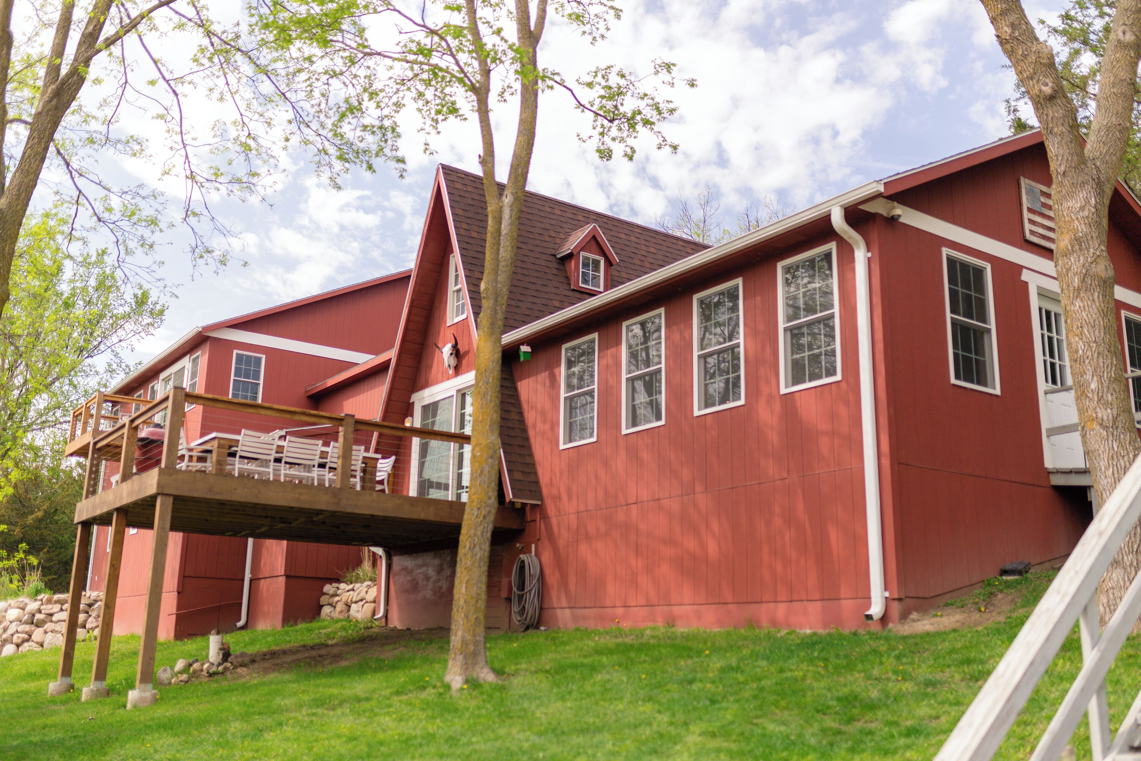 A red two-story house with a wooden deck and a stone wall.
