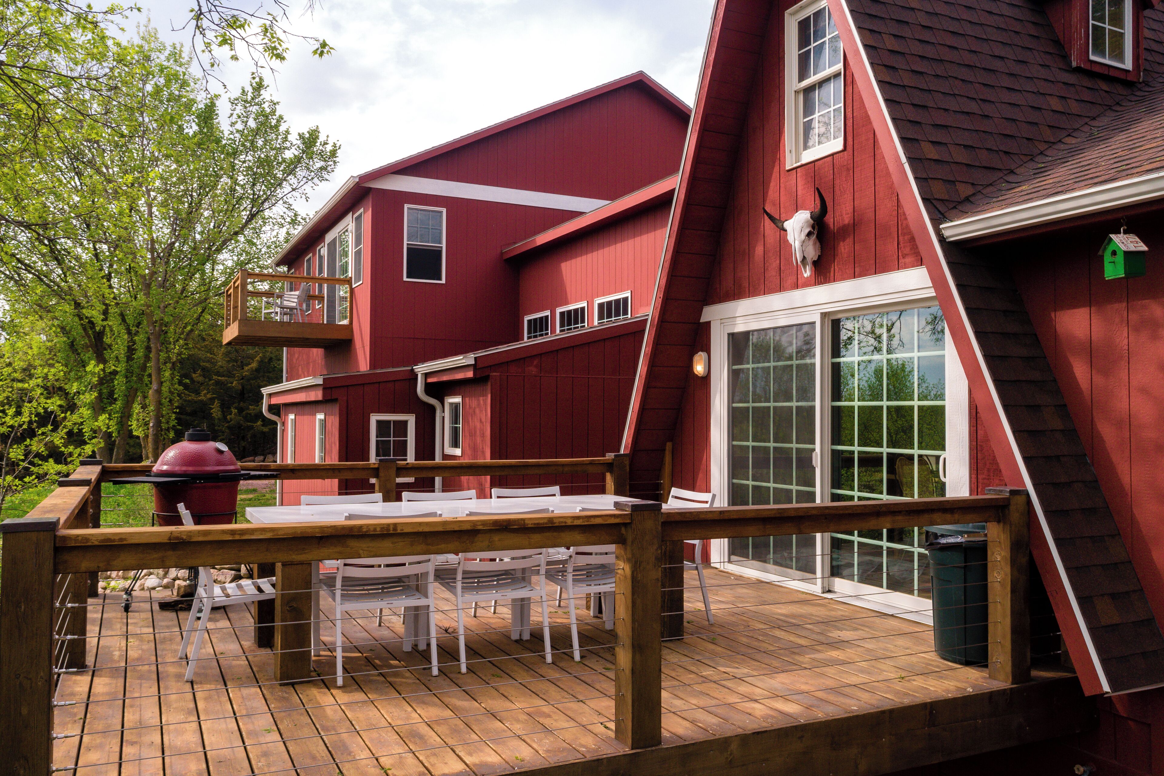 A red house with a deck, a barbecue, and a large window.