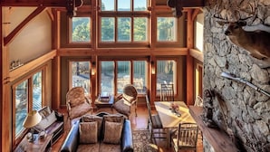 A spacious loft-style room with high ceilings, large windows, and a stone wall with antlers. - Luxury Lakeview Cabin with Hot Tub and Game Room! (Bryson City)