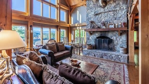 A spacious living room with a stone fireplace, large windows, and a cozy seating area. - Luxury Lakeview Cabin with Hot Tub and Game Room! (Bryson City)