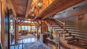 A spacious interior with a wooden staircase, a cozy seating area, and a large window providing natural light. - Luxury Lakeview Cabin with Hot Tub and Game Room! (Bryson City)