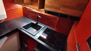 A kitchen with a black countertop, a double sink, a stove with four burners, and wooden cabinets. - Newly Renovated Apartment in Cervinia's Heart (Valtournenche)