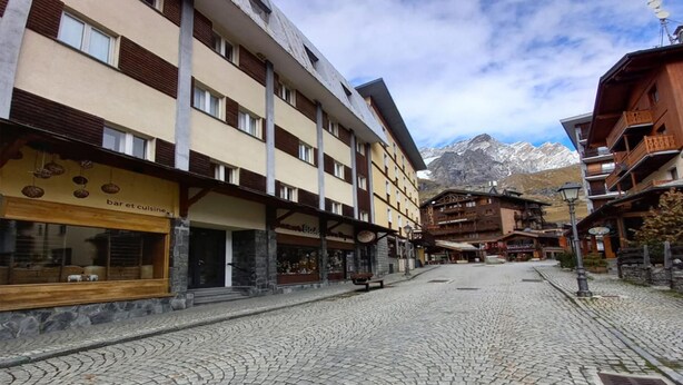 A cobblestone street lined with multi-story buildings, some with visible signage indicating shops and restaurants. - Newly Renovated Apartment in Cervinia's Heart (Valtournenche)