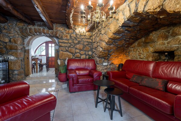 A cozy stone-walled room with leather sofas, a chandelier, and a fireplace.