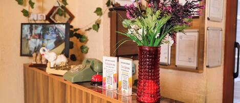 Un comptoir d’accueil orné d’un vase rouge rempli de fleurs, avec un téléphone et des panneaux d’information.